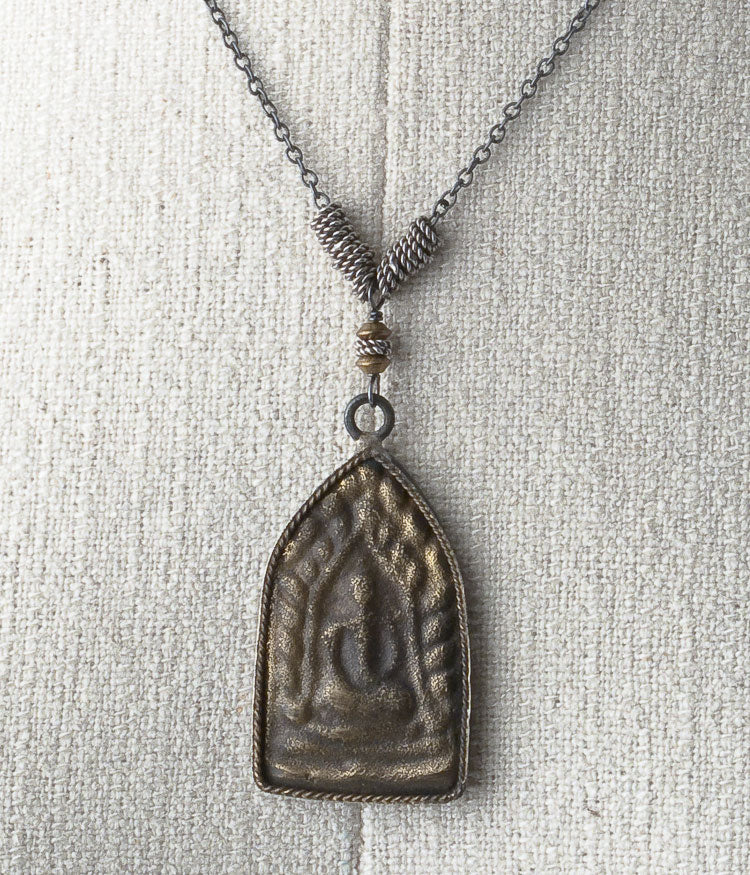 Brass, Balinese sterling, oxidized sterling silver.

This is a common shape in Thai amulets, as it mimics the architecture of a temple. This beautifully depicted sitting Buddha also has a lovely wheel emblem on the back - it is a connection to the spirit world. 

Necklace (adjustable), 18-20"
